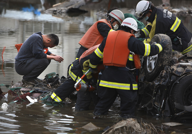 A Japanese man waits while Natori firefighters work to pry open his car to look for his missing family members after he found the family car in Natori, Japan, Monday. The firefighters found no one in the car. (Brian van der Brug/Los Angeles Times/MCT)