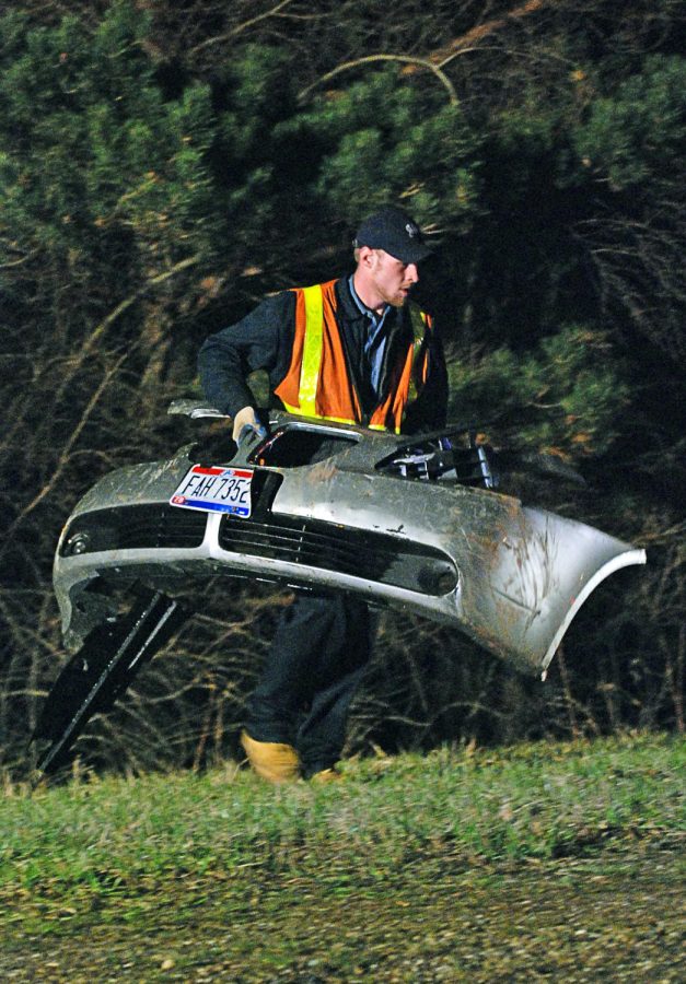 A worker from City Service Company carries the front bumper from a Pontiac G6 that went left of center on state Route 261 southbound Wednesday. Two passengers were in the vehicle that veered off into a ditch. Only minor injuries were reported . Photo by Matt Hafley.