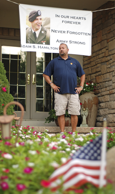 Scott Hamilton stands under the banner dedicated to his son on the front porch of his home. Scott said he kisses the banner every day when he leaves for work. Photo by Matt Hafley.