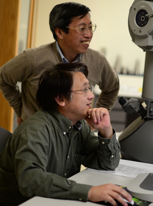 Qi-Huo Wei, associate professor of nano-biotechnology, examines the specimen in a microscope powerful enough to view a single atom, while Hiroshiv Yokoyama, director of the Liquid Crystals Institute, assists from over his shoulder. Photo by Jacob Byk.