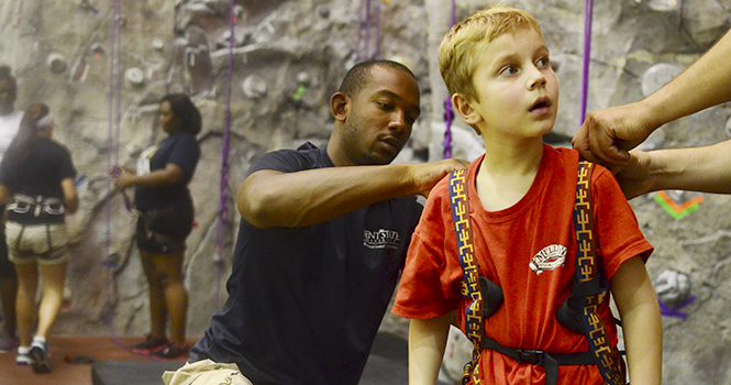 Desmond Bates, junior human development and family studies major, helps Emerson Puch, 7, of Hartville, get strapped in to climb the rockwall at the Rec Center on Sept. 14. Photo by Nancy Urchak.