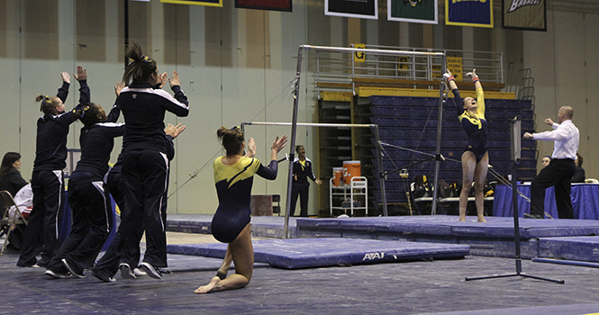The Kent State Gymnastics team cheer on senior Rachel Guida after her performance on the uneven bars Friday, Feb 15 at the MACC. KSU defeated Central Michigan 196.050 to 194.900. Photo by Shane Flanigan