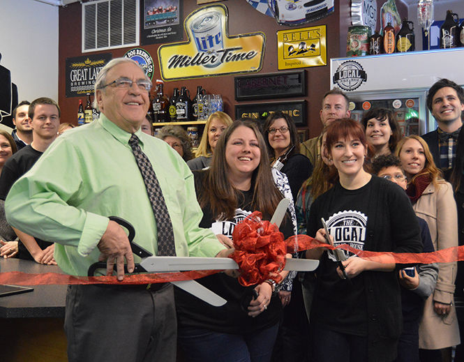 Mayor Jerry T. Fiala helps business owners Molly Taggart and Jen Cunningham cut the ribbon in honor of the opening of their new bar “The Local Public House,” in Kent on Feb. 3, 2014. Friends and locals gathered for the celebration and enjoyed free local soda on the house.