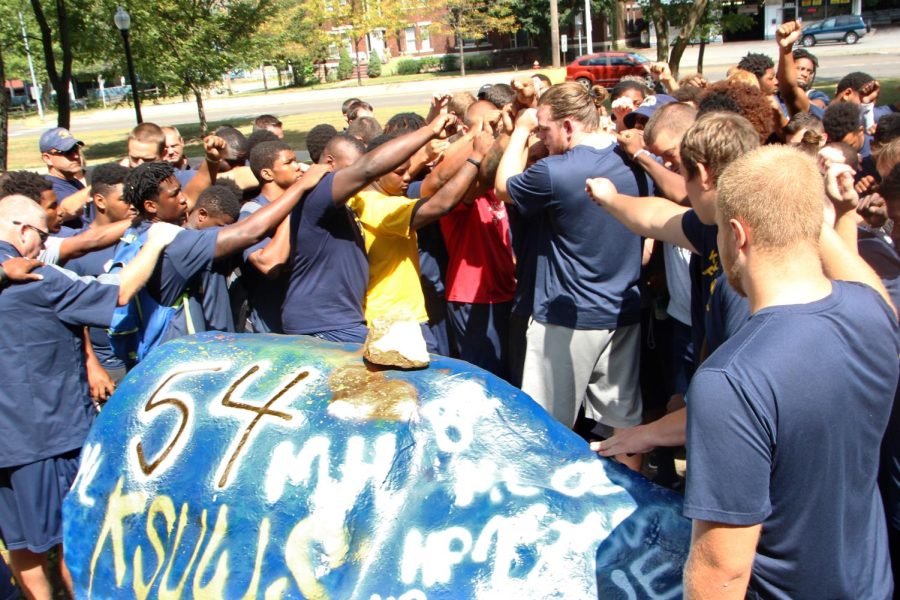 The Kent State football team does a team huddle and chant around the rock, which has Jason Bitsko’s football number 54 on it, on August 20, 2015. Kent State University is bringing back his number for the season. Junior left tackle Reno Reda will now be wearing his number.