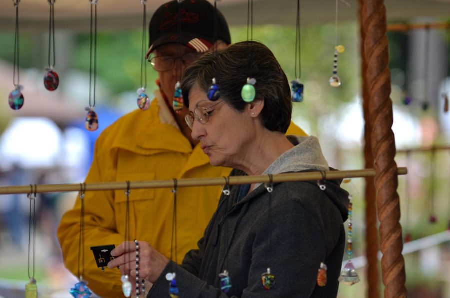 Kassi Jackson / The Kent Stater Ann Messino, Kent local, looks at a set of earrings while Joe Toporcer, of Crafter Glass at Earstone Jewelry based out of Youngstown, Ohio, talks to her about the piece at Art in the Park at Fred Fuller Park Saturday, Sept 12. 2015.