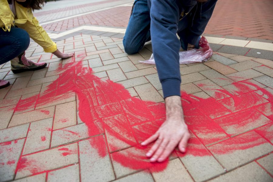 Vice President of Kents International Justice Mission student organization Delaney Cordova and architecture sophomore Nathaniel Williams spread red sand into the cracks of the K in the middle of Risman Plaza Wednesday March 1. The Red Sand Project was started by artist Molly Goochman to bring awareness to the human trafficking epidemic.