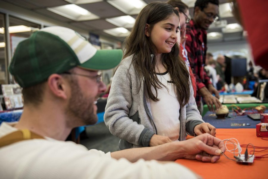 Anne Weber, 9, plays a game using physical contact as a controller with her father Michael Weber, a professor at Cuyahoga Community College and Lakeland Community College, at the Makey Makey table at Mini Maker Fair in the library Friday.