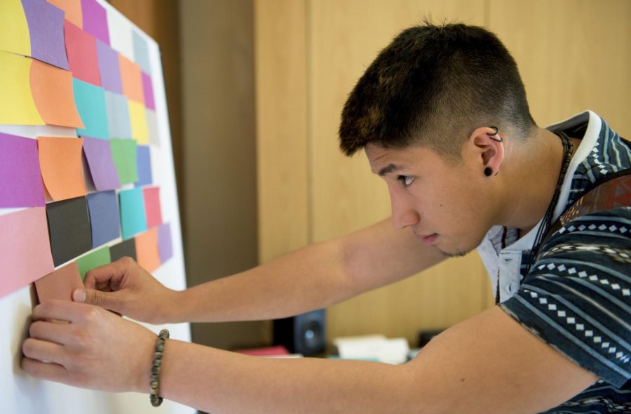 Translation major Carlos Usnay places a “brick” on the Oppression Wall in the student center on April 24, 2017. The wall remained standing for all of last week for students to add colored bricks representing different forms of oppression. At the end of the week, the wall will be torn down to tear down oppression. 