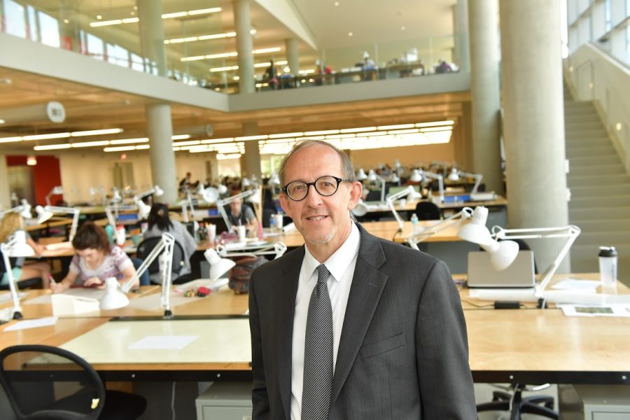 Mark Mistur, the dean of the College of Architecture and Environmental Design, poses for a photo in the building while architecture students behind him work.