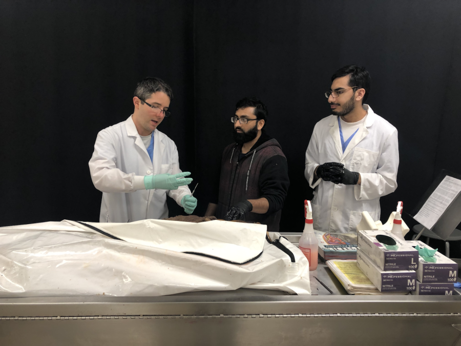 Morgan Chaney (left) demonstrates on a cadaver to his class and students Naeem Virk (middle) and Uzair Mumtaz (right) assist in the demonstration.