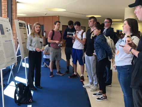 Katie Sheldon (left), a junior psychology major, presents her poster about a personality trait known as “grit” to a group of students at the Undergraduate Research Symposium on April 9.