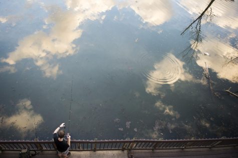 Clouds reflect off of the Cuyahoga River as a man fishes into on Feb. 24, 2017. The temperature reached into the seventies, unusually warm for February in Ohio.