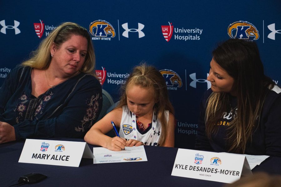 Coach Kyle DeSandes-Moyer (right) helps Mary Alice Tryda (center) as she signs on to the Kent State Golden Flashes Field Hockey team, at the Mac Center, while her mother Kelly Tryda (left) watches on. Sept. 25, 2019.