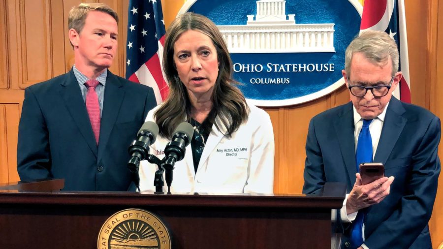 Dr. Amy Acton, the director of the Ohio Department of Health, center, discusses the confirmation of Ohios first three cases of coronavirus, as Gov. Mike DeWine, right, studies an update on the cases provided to him during a news conference, Monday, March 9, 2020, in Columbus, Ohio. Lt. Gov. Jon Husted is at left. Acton said the state is leaning in and taking an aggressive approach to combating the disease. (AP Photo/Andrew Welsh-Huggins)