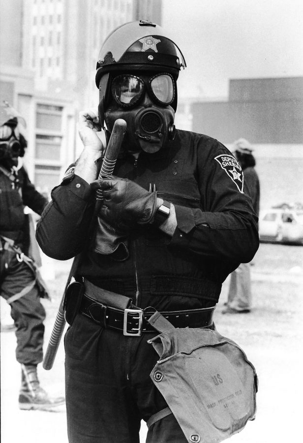 A Portage County deputy sheriff straps on a gas mask during protests at Kent State University over the Gym Annex construction project, October 22, 1977. Police launched tear gas at the protesters and made several arrests.