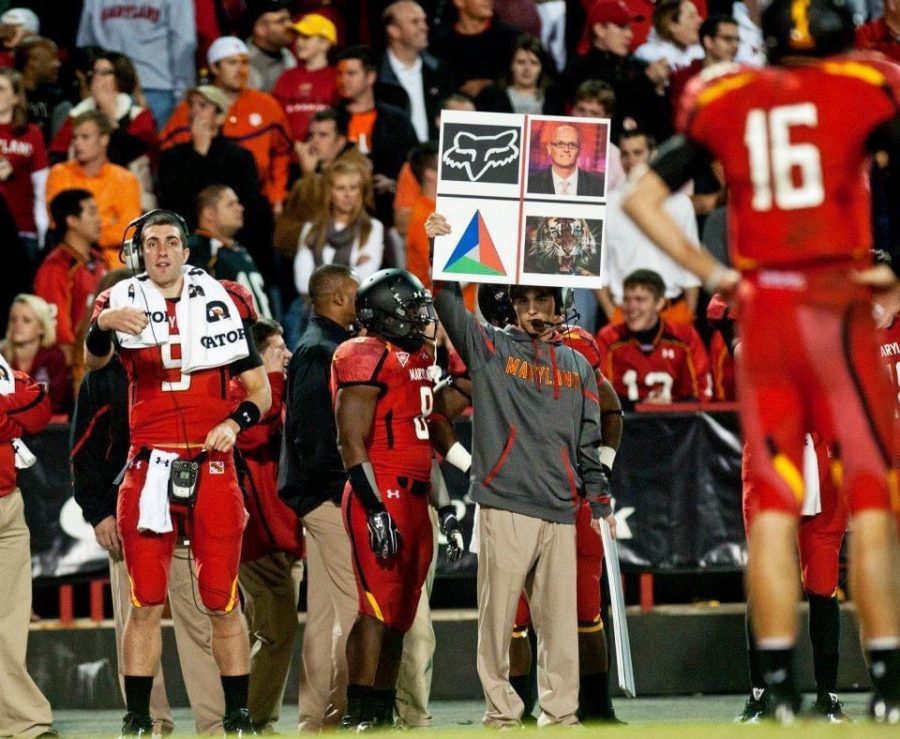 Schrum+holds+up+a+play+calling+sign+on+the+sideline+of+a+game+at+Maryland+in+2011.