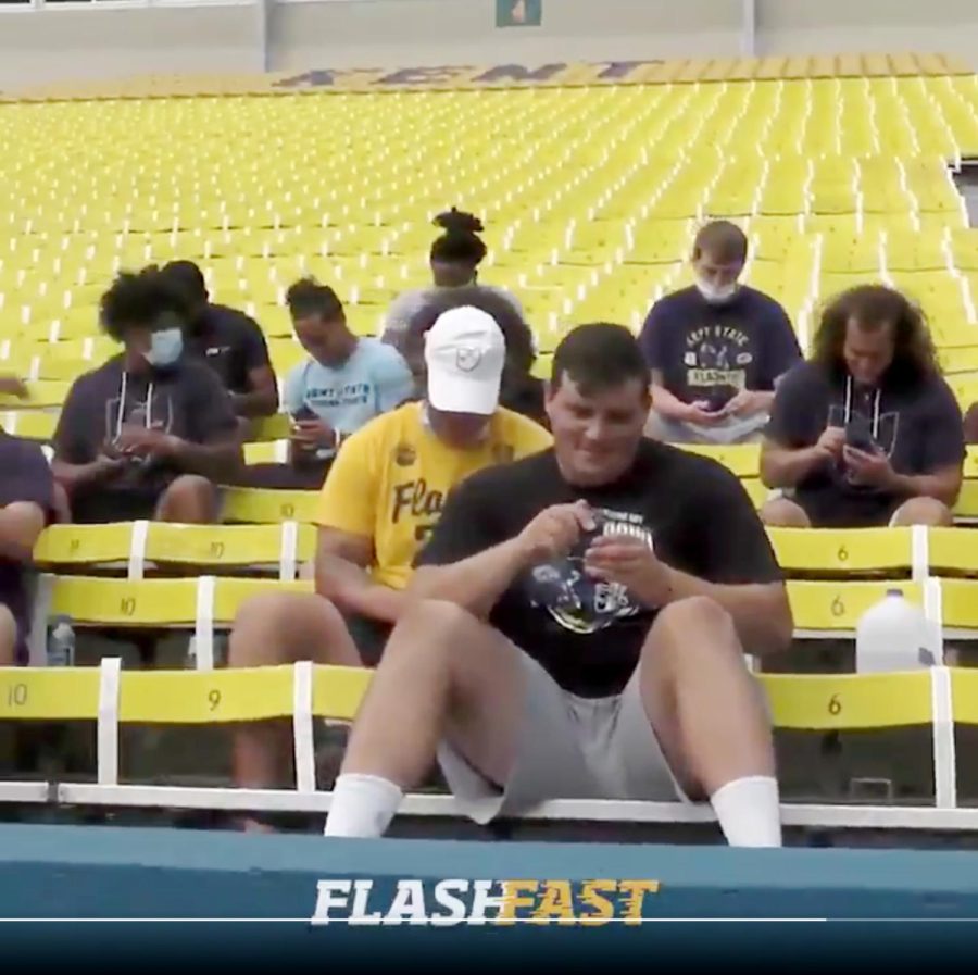 Kent State football players sit in the stands, admiring the rings. Many appear not be wearing a mask. 