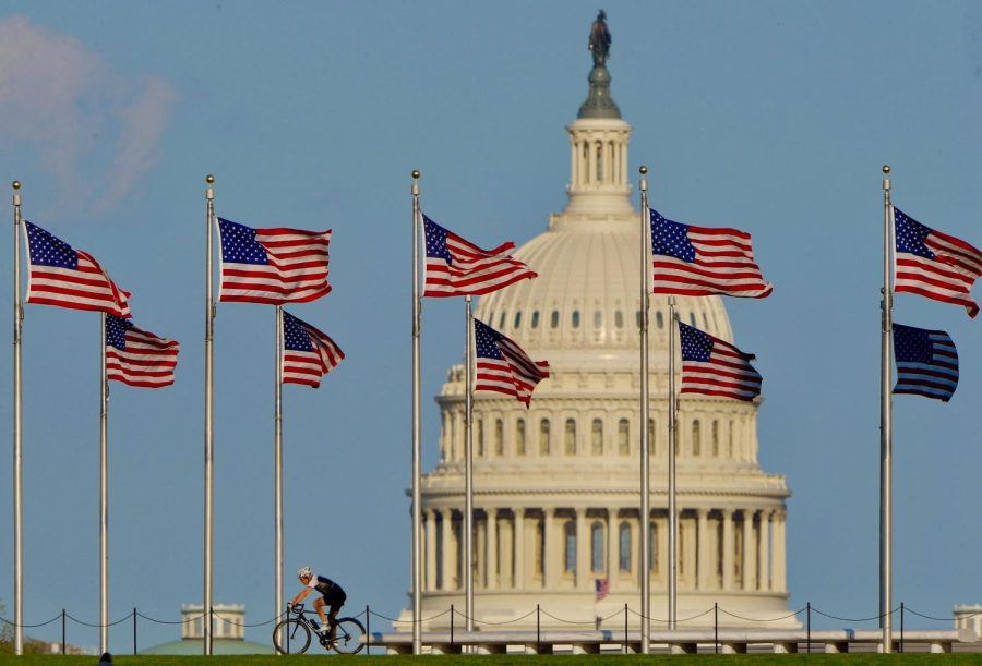 WASHINGTON, DC - APRIL 8: A lone bicyclist rides under the circle of flags surrounding the Washington Monument, the United States Capitol is prominent in the background. 