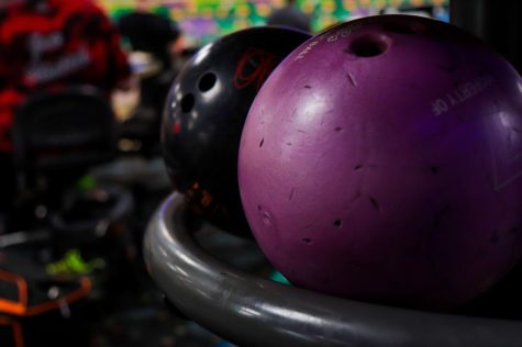 Bowling balls sit on the shelf at Kent Lanes while bowlers sit and eat appetizers waiting for their turn to bowl.