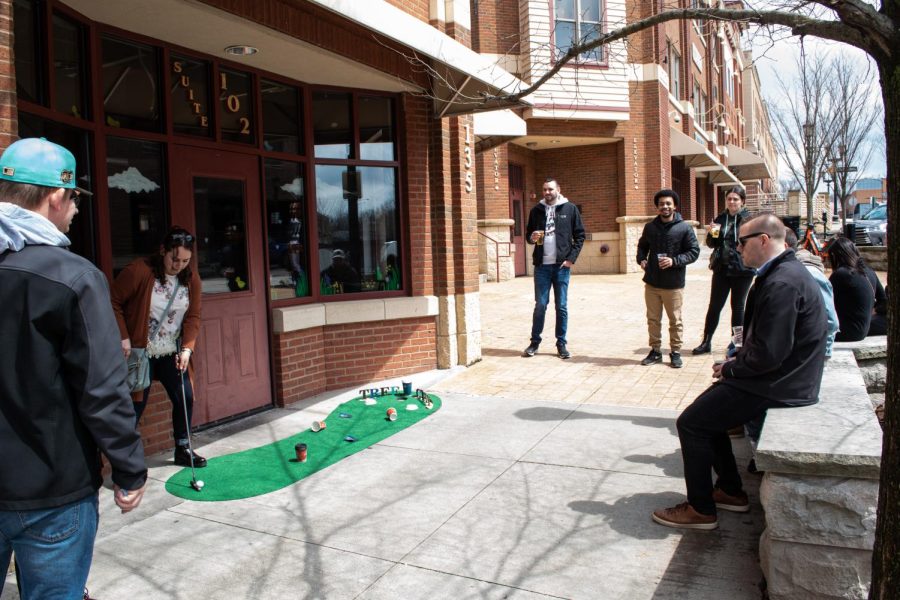 A group of people take turns putting at Tree City Coffees miniature golf course.