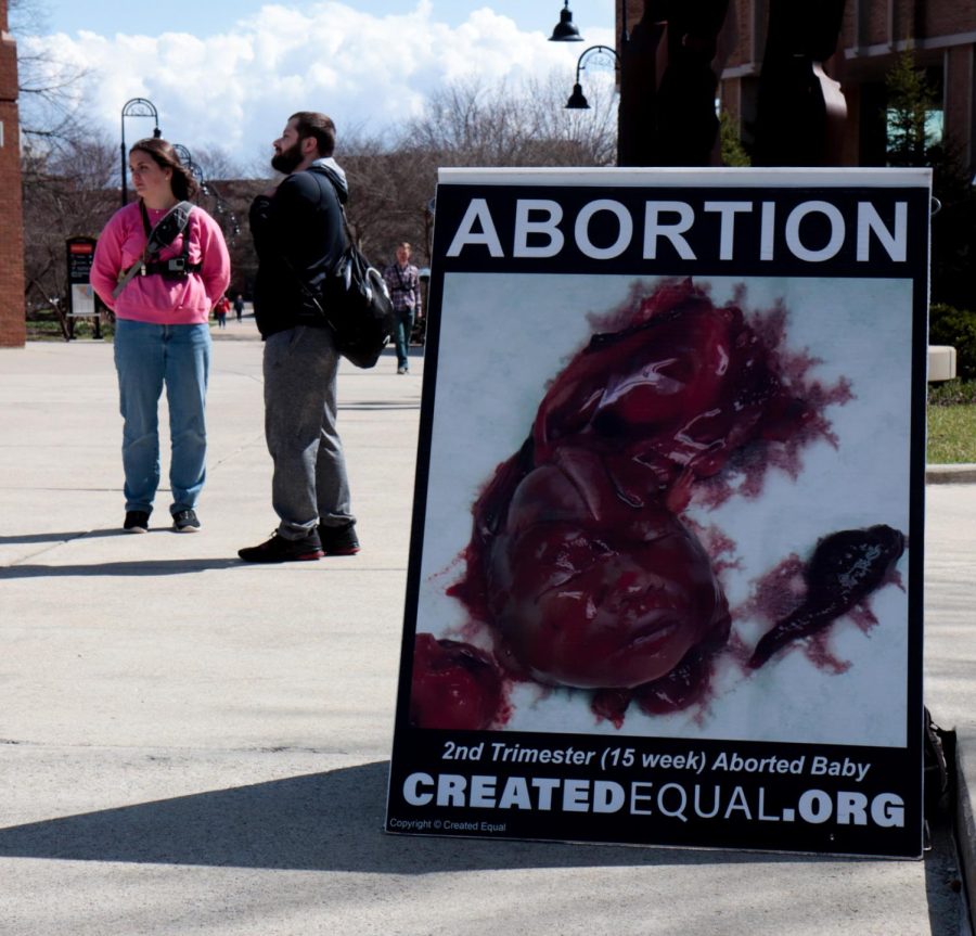 Mya, pictured on the left, stands and talks with a student behind one of their signs showing a baby after an abortion at the anti-abortion demonstration on the K on Thursday, April 7.