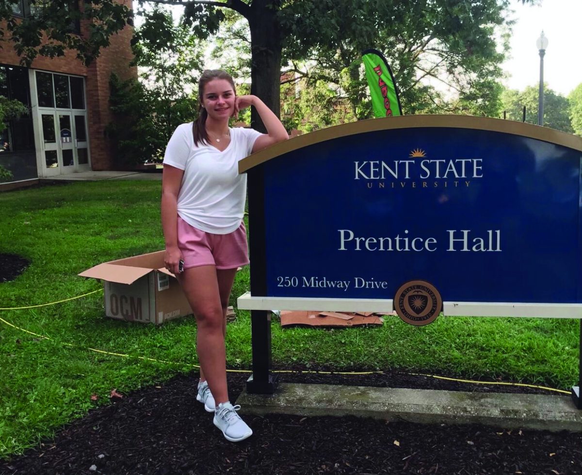 Erin Sullivan, a journalism major now in her fifth year at Kent State, stands in front of the sign to her freshman year dorm building in 2019. 