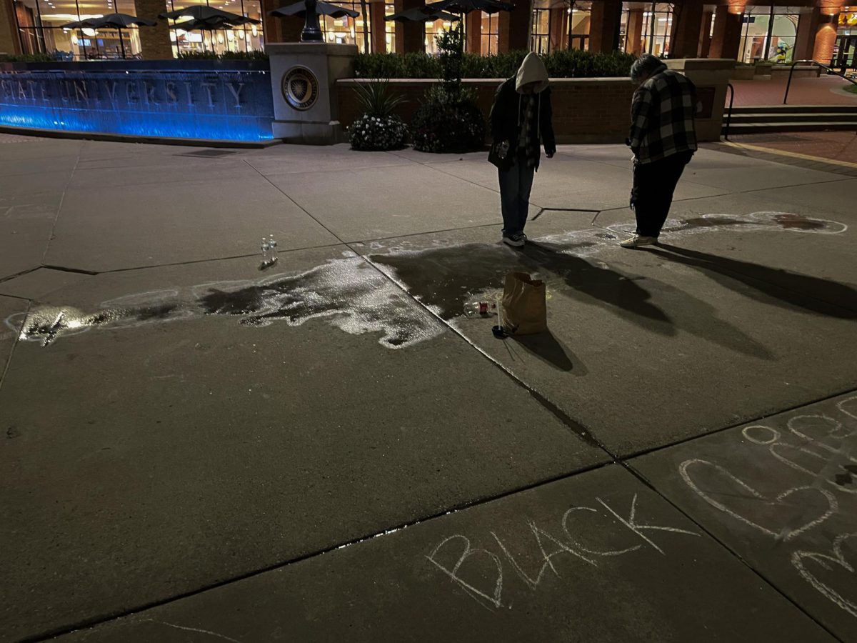 Kent State students erase chalk writing on the K speaking out against voting Yes on Issue 1 with bottles of water on Oct. 18, 2023.