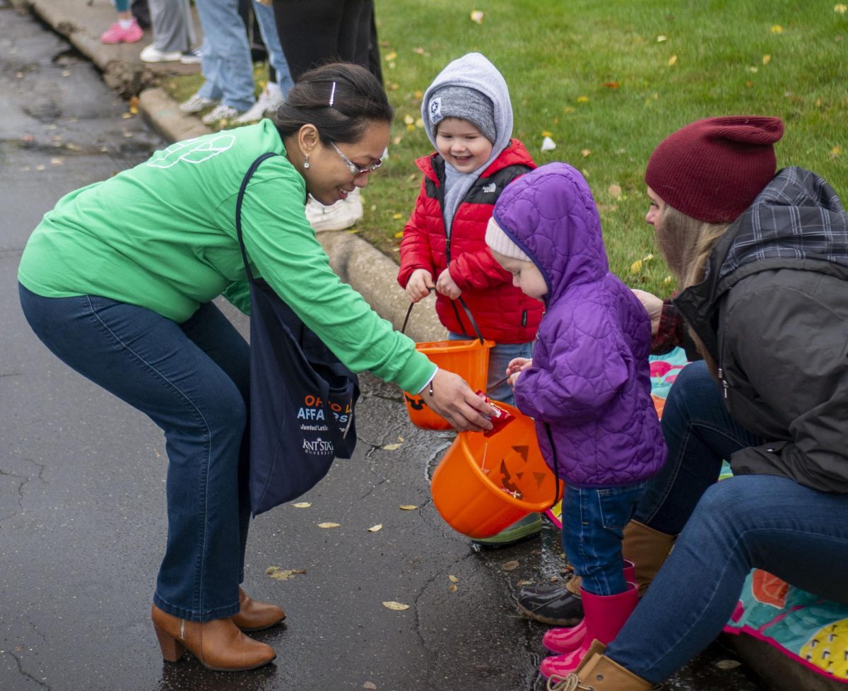 Department of Physics Administrative Secretary Jenefer Villanueva, walking with Kent State of Well-being, hands out candy to children watching the 2023 Homecoming Parade on Oct. 21, 2023.