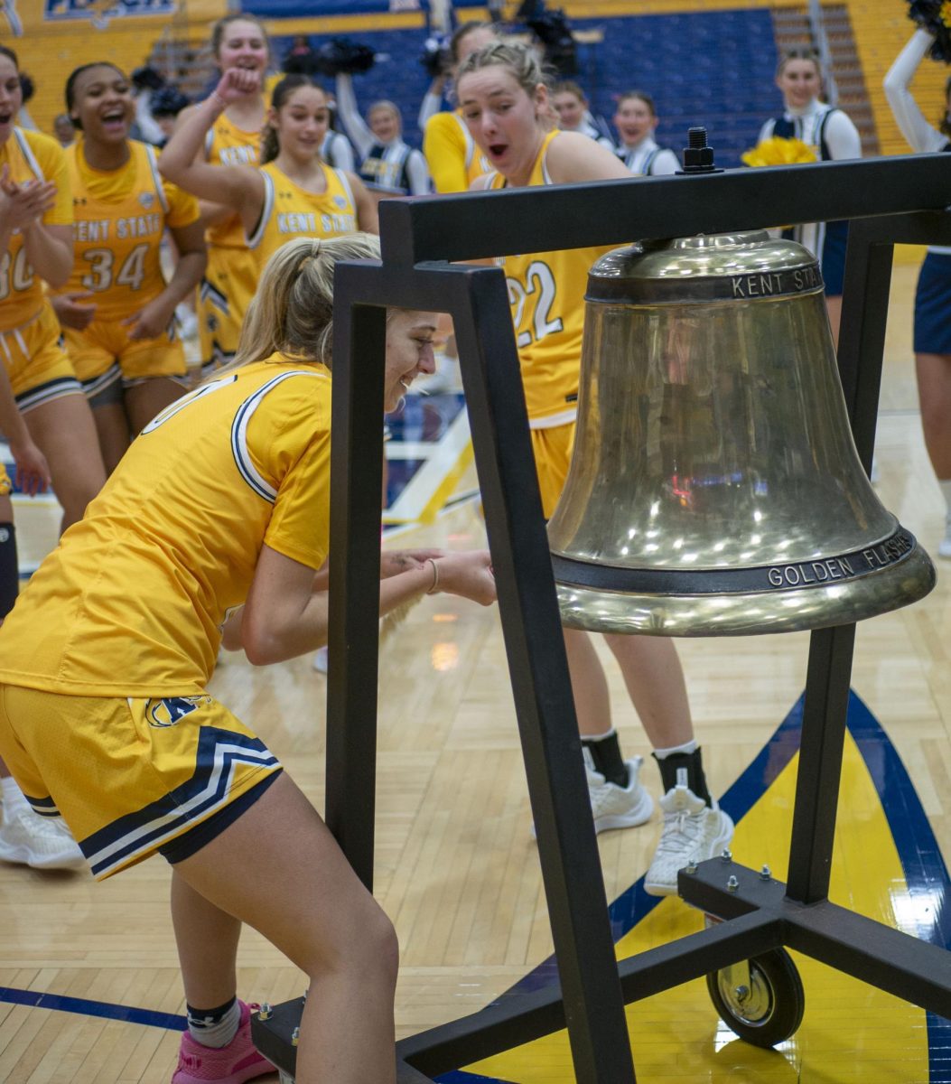 Redshirt sophomore guard Kaley Perkins rings the Starner Victory Bell, with graduate student guard Abby Ogle and the team cheering her on, after following the Golden Flashes 109-31 win over LaRoche on Dec. 30, 2023. Perkins, a transfer from Oklahoma, netted her season high in minutes, rebounds, blocks and made field goals in the game and was selected by the team to ring the bell.