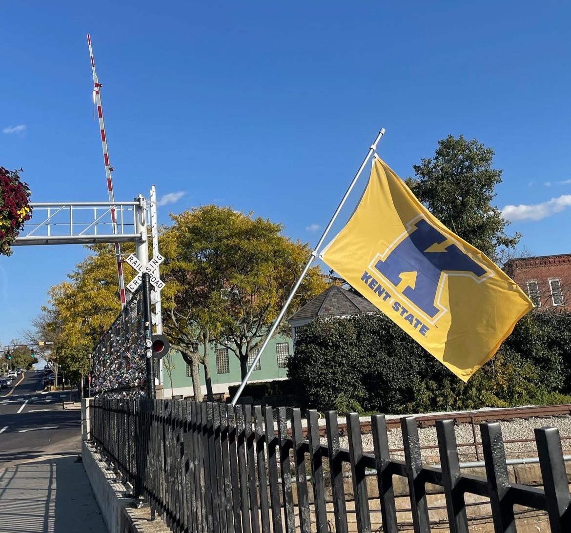 A Kent State University flag in the foreground with the Lock Bridge in the background.