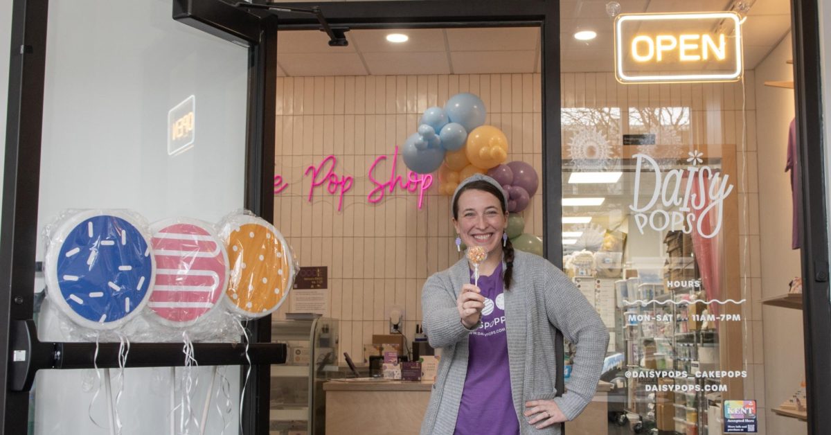 Amy Mucha stands in the doorway of her shop, Daisy Pops, with her favorite cake pop, Fruity Pebbles. Mucha retired from teaching in 2021 from Cuyahoga Valley Christian Academy to open her shop less than a year ago.  