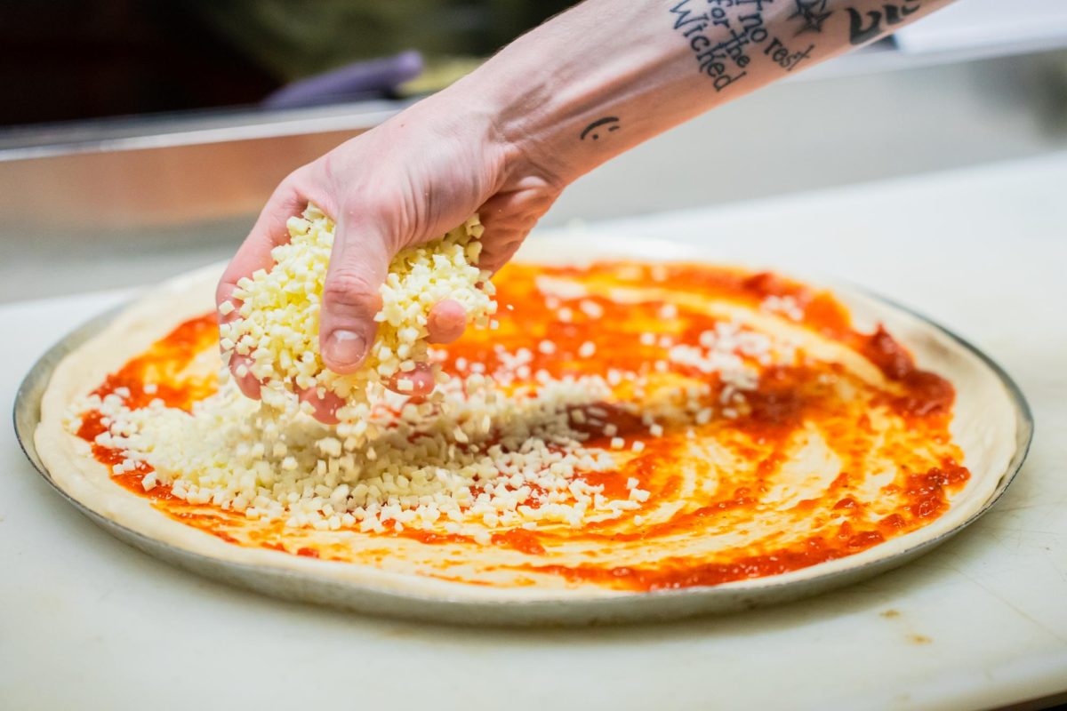 A employee of Guys Pizza Co. sprinkles cheese on a pizza.