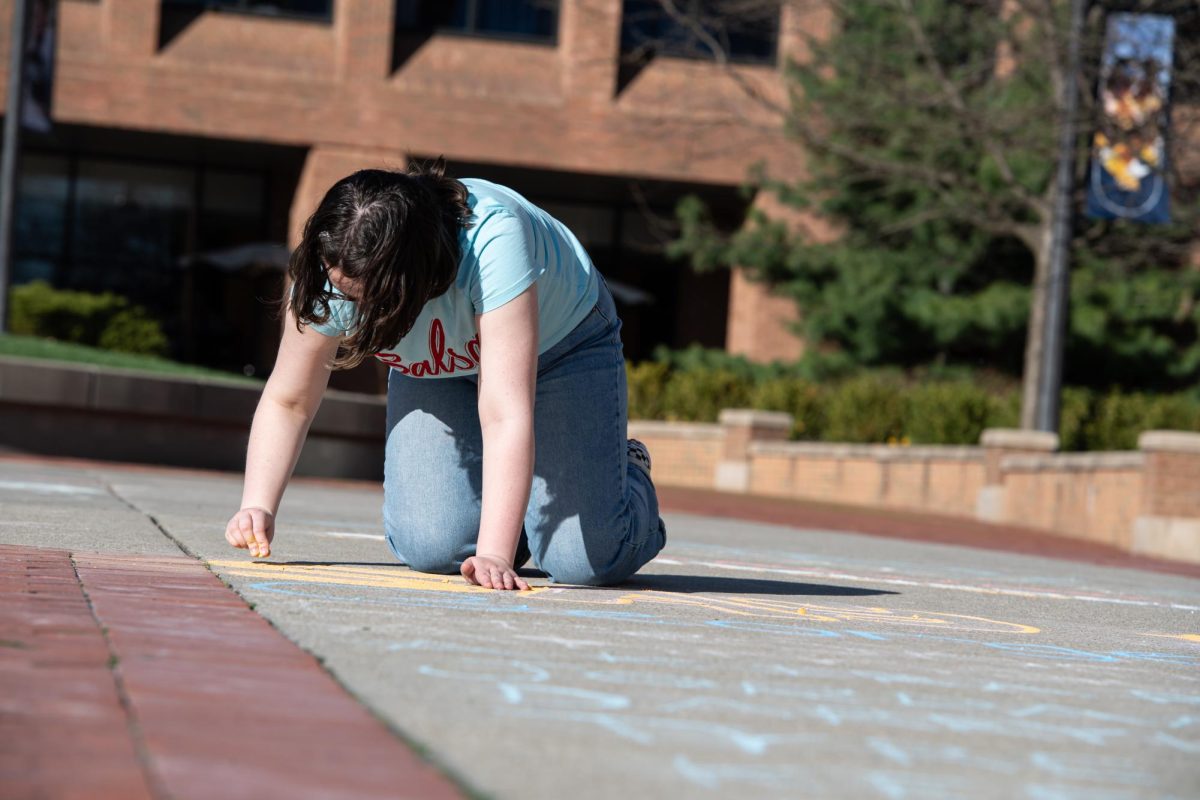 Junior anthropology major Nica-Emmanuel Delgado, vice-president of SALSA, uses chalk to write down the names people of color who have lost their lives to hate crimes during the protest April 15, 2024. 