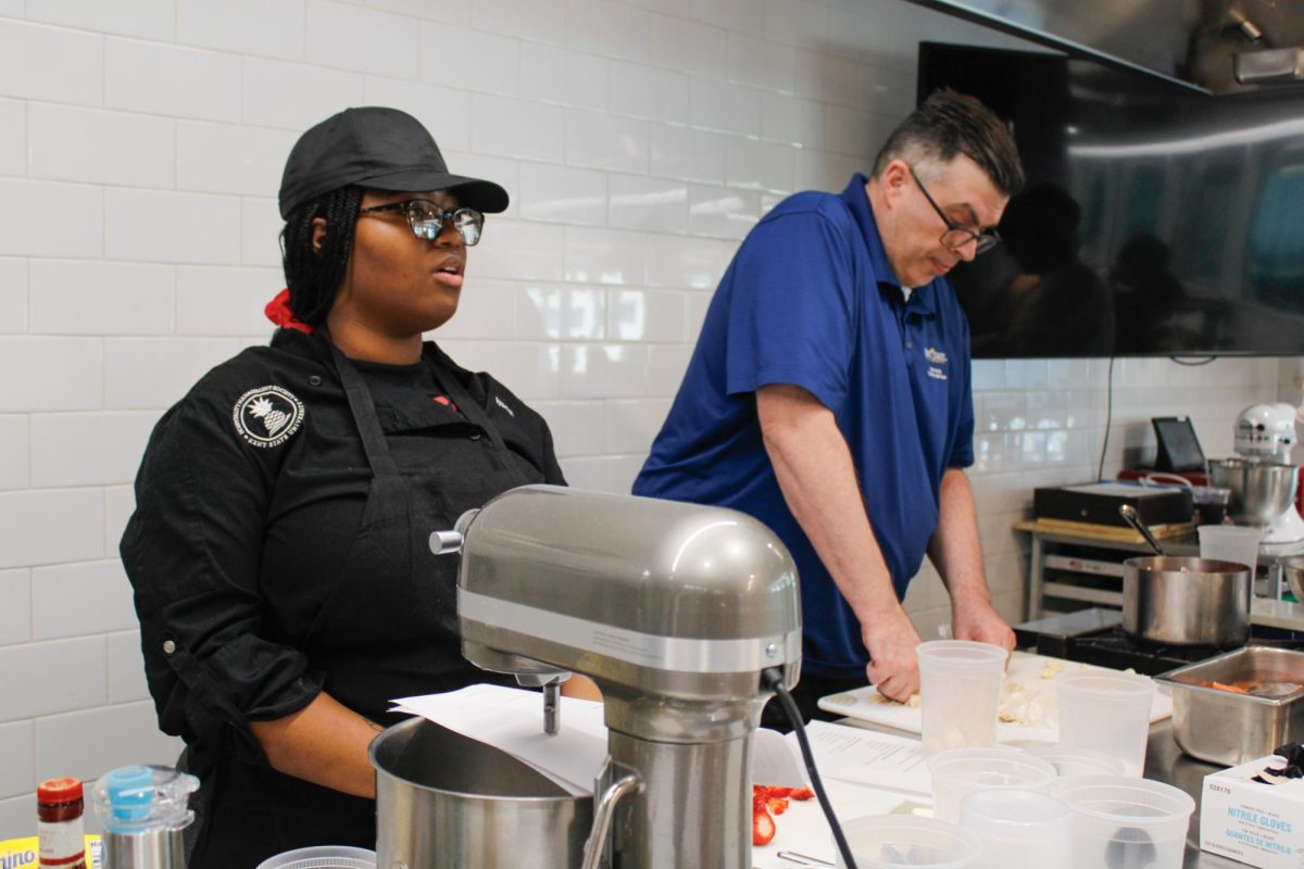 Senior, Iyaelah Thompson and Professor Christian Booher cut up food for their recipes during a culinary class in the DI Hub on September 13, 2024