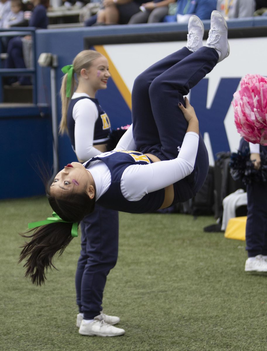 On the sidelines at the football game against Ball State University, a cheerleader performs a backflip.